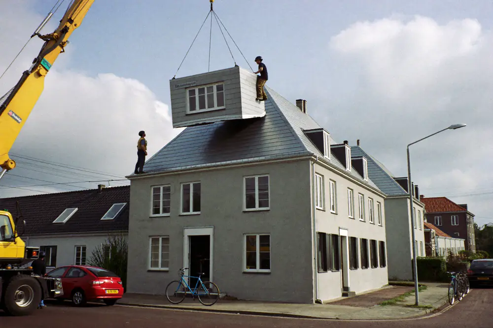 Een prefab dakkapel wordt met een kraan op het dak van een woning in een rustige straat getild